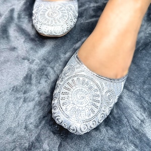 May include: A pair of silver embroidered flat shoes with a floral design. The shoes are made of a soft, comfortable material and have a pointed toe.