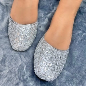 May include: A pair of silver sequined flat shoes. The shoes have a pointed toe and are decorated with small, round sequins.