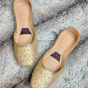 K&ouml;nnte beinhalten: Ein Paar flache goldene Schuhe mit spitzen Zehen, verziert mit Pailletten. Die Schuhe haben ein Obermaterial aus goldenem Leder mit einem zarten Muster aus Pailletten. Der Markenname "London Look" ist auf der Innenseite der Schuhe aufgedruckt.