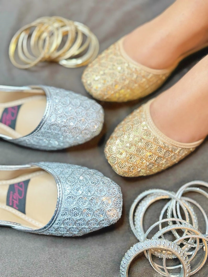 May include: Two pairs of flat shoes with gold and silver sequins. The shoes are decorated with small round sequins. The shoes are surrounded by gold and silver bangles.