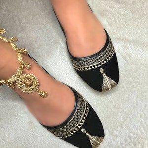 Op de afbeelding: Zwarte fluwelen ballerina's met gouden borduurwerk en kwastjes. De schoenen hebben een spitse neus en een lage hak.