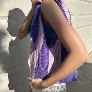 May include: A purple and pink striped crocheted tote bag with a wide strap.