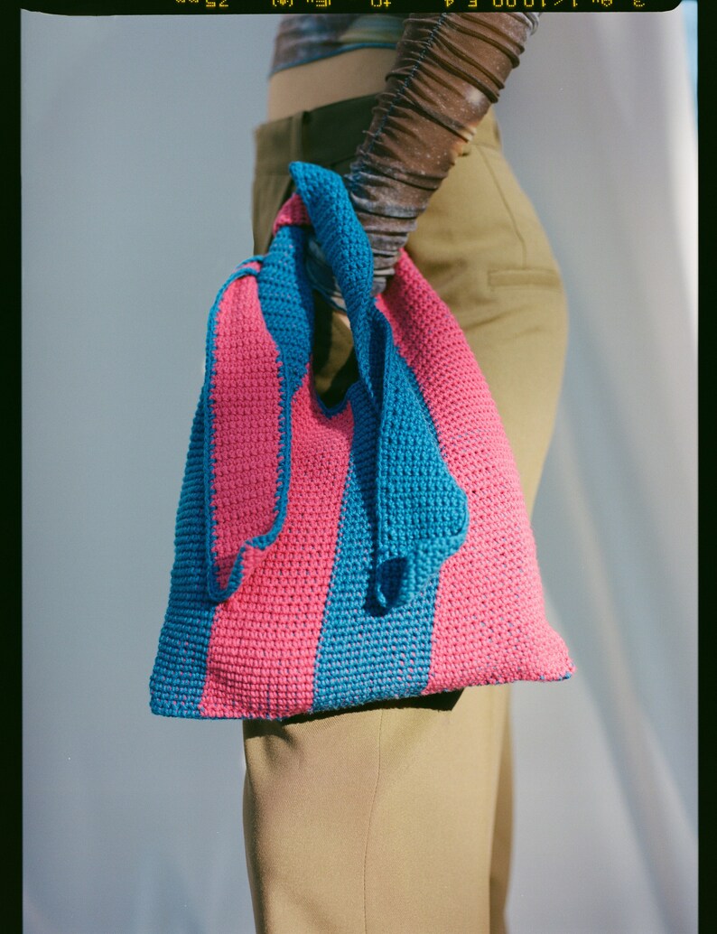 May include: A pink and blue striped crocheted tote bag with a knotted handle.