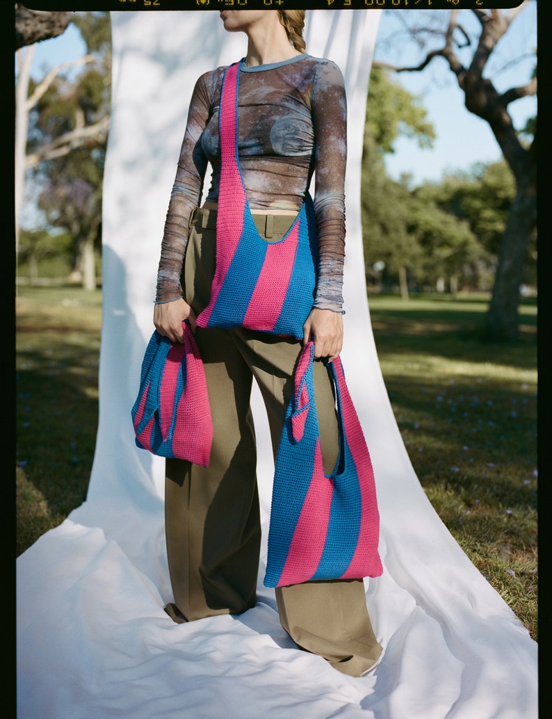 May include: Two pink and blue striped crocheted tote bags. The larger bag is worn over the shoulder and the smaller bag is held in the hand.