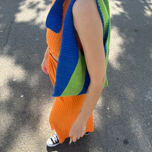 May include: A blue and green striped crocheted bag worn over the shoulder of a person wearing an orange dress.