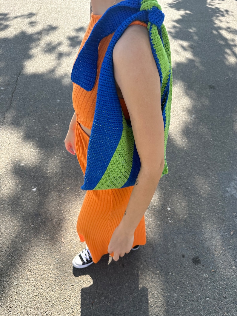 May include: A blue and green striped crocheted bag worn over the shoulder of a person wearing an orange dress.