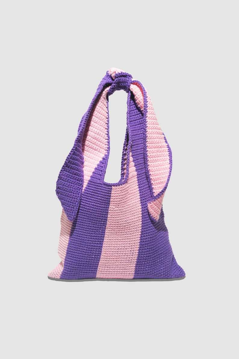 May include: A purple and pink striped crocheted tote bag with a knotted handle.