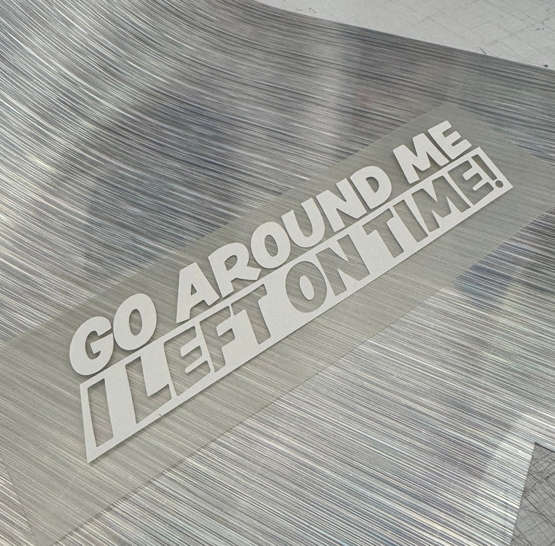 May include: White vinyl sticker with the text "Go Around Me I Left On Time!" on a silver background.