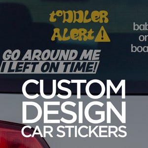 May include: A white car with a black rear window. The window has a yellow and black sticker that says "Toddler Alert!" and a gray sticker that says "Go Around Me I Left On Time!" There is also a gray sticker that says "baby on board". The car has a white sticker that says "CUSTOM DESIGN CAR STICKERS".