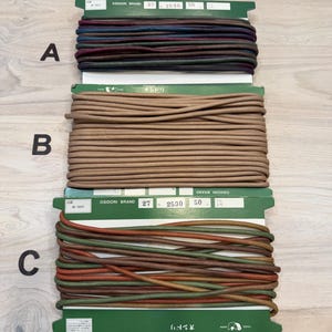 May include: Three spools of cord in varying colors. The top spool features dark red, blue, and green cords. The middle spool is a solid tan color. The bottom spool has a mix of green, orange, and brown cords. Each spool is labeled with the "OSIDORI BRAND" logo.