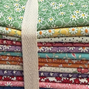 May include: A stack of colorful fabric squares, bound with a cream-colored ribbon. The fabrics feature floral patterns in various colors, including green, yellow, pink, and blue. The daisy and floral prints are visible on the stacked fabric.
