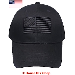 May include: A solid black baseball cap featuring a tonal, embroidered American flag patch centered on the front panel. The cap has a structured crown, a curved brim, and stitched eyelets for ventilation, presenting a monochromatic design.