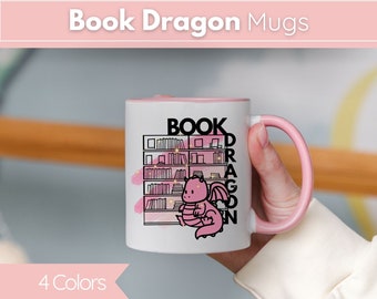 May include: A white ceramic mug with a pink rim and handle. The mug features a pink dragon with a bookshelf behind it and the text "BOOK DRAGON" in black.