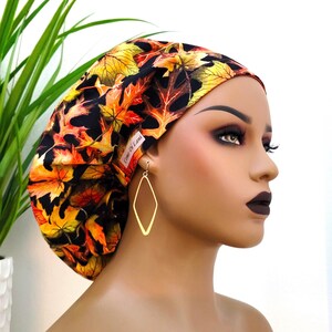 May include: A black, orange, and yellow surgical cap with a fall leaf print. The cap has a label that says "Cami Di Lani".