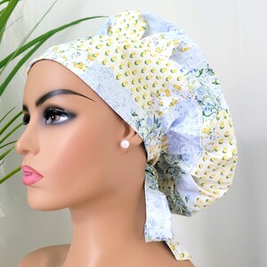 May include: A floral patterned bonnet in shades of yellow, blue, and white. The bonnet features a patchwork design with a mix of floral and botanical prints. The fabric is soft and appears to be cotton. The bonnet is tied at the back.