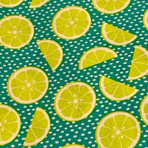 Puede incluir: Una tela de color turquesa con un patrón de lunares blancos y una imagen repetida de limones amarillos. Los limones están cortados por la mitad y dispuestos en un patrón circular.