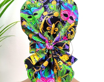 May include: A colorful scrub cap featuring a vibrant Mardi Gras theme. The cap showcases a black background adorned with masks, fleur-de-lis, and peacock feathers in green, purple, pink, and gold. A large bow adds a decorative touch.