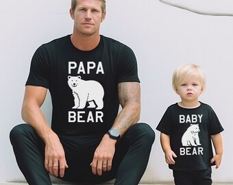 May include: Matching black t-shirts with white bear graphics and text. One shirt says "PAPA BEAR" and the other says "BABY BEAR". The shirts are worn by a man and a child, suggesting a family theme.