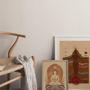 May include: Two framed illustrations of a woman in a seated pose with a sun and moon symbol above her head. The illustrations are on a beige background with brown and red accents. The illustrations are framed in white and wood frames.