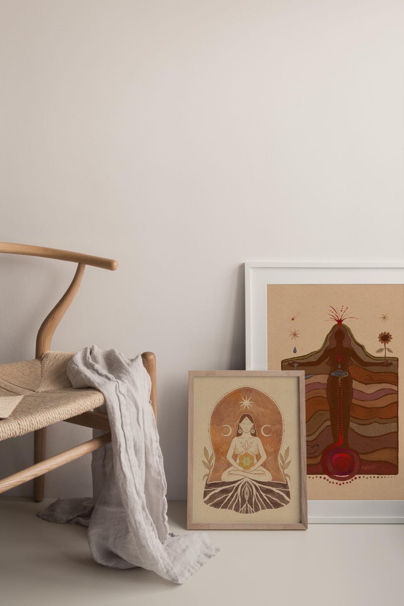 May include: Two framed illustrations of a woman in a seated pose with a sun and moon symbol above her head. The illustrations are on a beige background with brown and red accents. The illustrations are framed in white and wood frames.