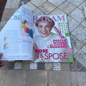 May include: A magazine cover featuring a woman with blonde hair wearing a white dress and a pearl necklace. The magazine is titled "Rose & Spose" and has a pink and green color scheme. The cover also features a poster of flowers with the text "Poster in Fiore da Appendere & Ricamare".