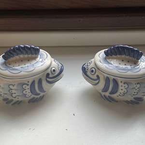 Puede incluir: Dos saleros y pimenteros de cerámica con forma de pez con diseños pintados en azul y blanco. Los saleros tienen tapas y se enfrentan.