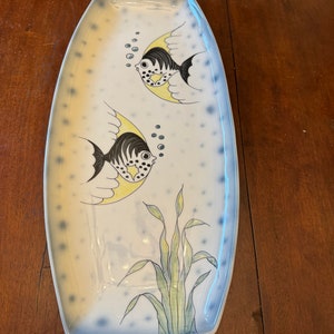 May include: A white ceramic serving platter with a blue rim and a design of two black and white fish with yellow fins and seaweed. The fish are swimming in a blue and white background with white dots.