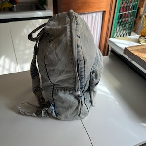 May include: A light blue denim backpack with a zipper closure and a small pocket on the front.