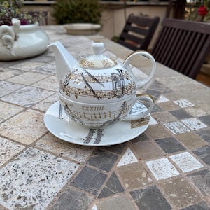 Peut inclure: Un service à thé en porcelaine blanche orné de notes de musique et d'instruments. L'ensemble comprend une théière, une tasse et une soucoupe, toutes ornées de détails dorés. La théière et la tasse sont décorées de partitions musicales et d'instruments à vent.