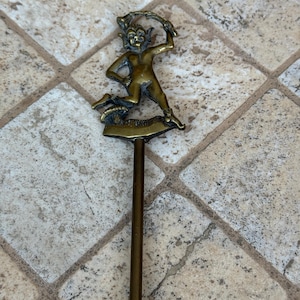 May include: A brass fireplace poker with a detailed figurine of a goblin holding a stick. The goblin is standing on a small base.