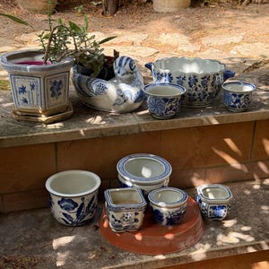 May include: A collection of blue and white ceramic planters and bowls featuring various floral and botanical patterns. The set includes a duck-shaped planter, a large scalloped bowl, and several smaller square and round pots of different sizes.