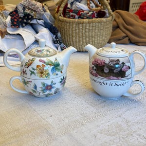 Peut inclure: Deux tasses à thé et théières blanches avec des motifs décoratifs. L'une présente des fleurs et des papillons colorés, l'autre un panier de chatons et le texte "A Very Fine Cat brought it back!"