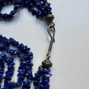 Peut inclure: Un collier multi-rangs composé de petites perles de lapis-lazuli bleu foncé irrégulières. Le collier a un fermoir argenté et deux perles argentées.
