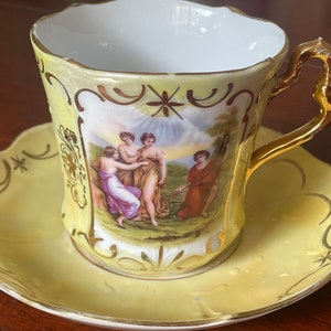 Könnte beinhalten: Ein gelbes Tee-Set mit goldenen Verzierungen und einer gemalten Szene mit drei Figuren in einer Landschaft.