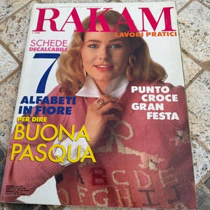 May include: A magazine cover featuring a woman wearing a pink knitted sweater with a white collar. The magazine is titled "Rakam" and features the text "Schede Decalcabili" and "Alfabeti in Fiore per dire Buona Pasqua".