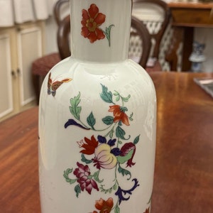 May include: A white porcelain vase with a gold rim and floral designs in shades of red, orange, yellow, green, blue, and purple. The vase features a butterfly design.