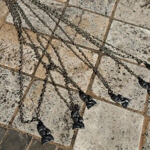 May include: Several silver-toned necklaces with pendant charms featuring a mother and child design. The necklaces are laid out on a stone tile surface, showcasing the intricate details of the pendants and chains.