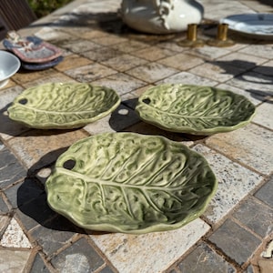 Peut inclure: Trois plats de service en céramique en forme de feuille de chou vert sur une surface carrelée.