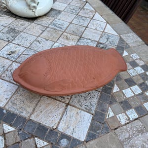 Könnte beinhalten: Eine terrakottafarbene, fischförmige Servierplatte mit detaillierten Schuppen- und Flossendesigns. Die Platte hat eine warme, rötlich-braune Farbe und scheint aus Ton zu sein. Das Wort "VENTO" ist sichtbar.