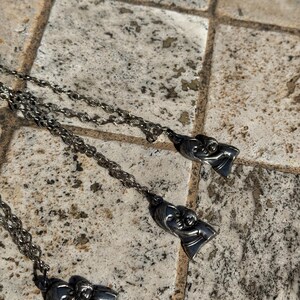 May include: Three silver-toned necklaces with pendant charms. Each charm depicts a mother and child in a loving embrace. The chains have a delicate, twisted design. The necklaces are displayed on a textured, neutral-toned surface.