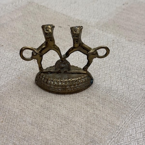 Puede incluir: Una pequeña escultura de metal dorado de dos leones de pie sobre sus patas traseras, frente a frente. Los leones sostienen un anillo en sus patas. La escultura está sentada sobre una pequeña base redonda.