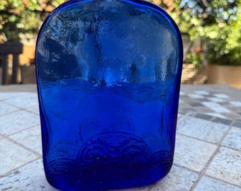 Botella vintage de vidrio prensado azul cobalto (azul rey), plana, con flores en relieve. Botella para elixir. Vidrios de Levante, España.