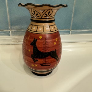 Może przedstawiać: Brązowy ceramiczny wazon z czarnym wzorem jelenia i złotymi akcentami. Wazon ma falisty brzeg i czarno-biały geometryczny wzór wokół górnej części.