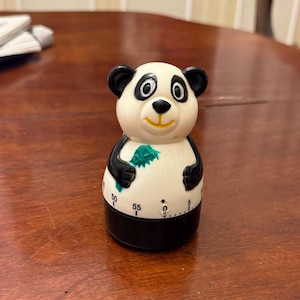 Peut inclure: Un minuteur de cuisine en forme de panda noir et blanc tenant une feuille verte dans sa main. Le minuteur a un cadran avec des chiffres de 0 à 60.