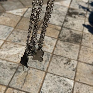 May include: Silver-toned layered necklace with small, delicate chains. The necklace features two pendant charms, one shaped like a butterfly and the other like a bird. The jewelry is displayed against a neutral background.