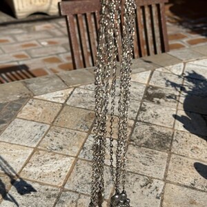 May include: Silver-toned necklaces with delicate chain links and decorative pendants. One pendant features a leaf design, while the other showcases a cluster of small, round shapes. The necklaces hang against a neutral background.