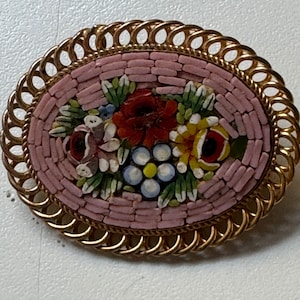 May include: A pink and gold oval brooch with a floral mosaic design. The mosaic features a variety of flowers in shades of red, yellow, blue, and green.