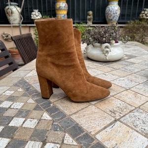 May include: A pair of brown suede ankle boots with a block heel. The boots have a pointed toe and a zipper on the inside of the ankle.