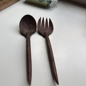 May include: A set of two brown coconut shell utensils, a spoon and a fork, on a white surface.