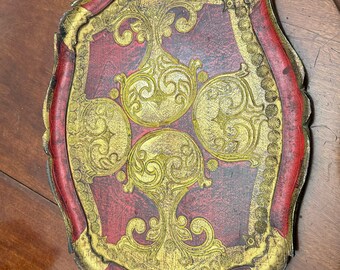 May include: An oval-shaped serving tray with a red and gold finish. The tray has a decorative design with intricate swirls and flourishes. The tray has a raised edge and two handles.